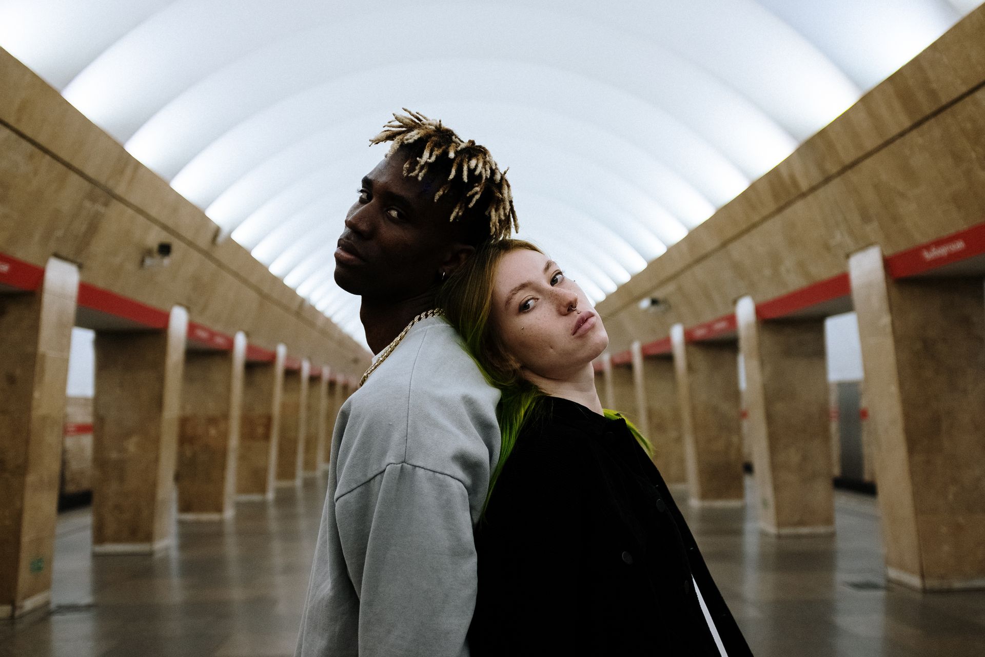 Young couple standing back to back in a modern subway station, embodying urban style.