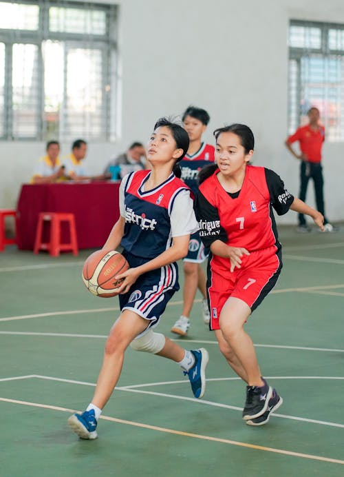 Full body of Asian women team in uniform playing basketball game in hall
