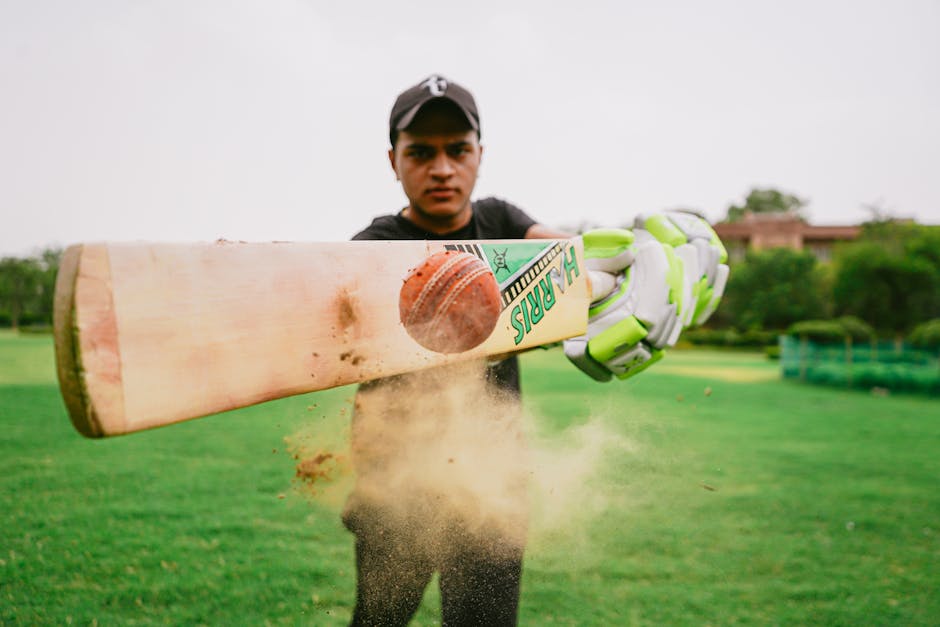Closeup of cricket bat and ball hit by sportsman wearing sportswear and gloves on blurred background