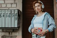 Female in vintage outfit listening to music in headphones while standing against entrance of building