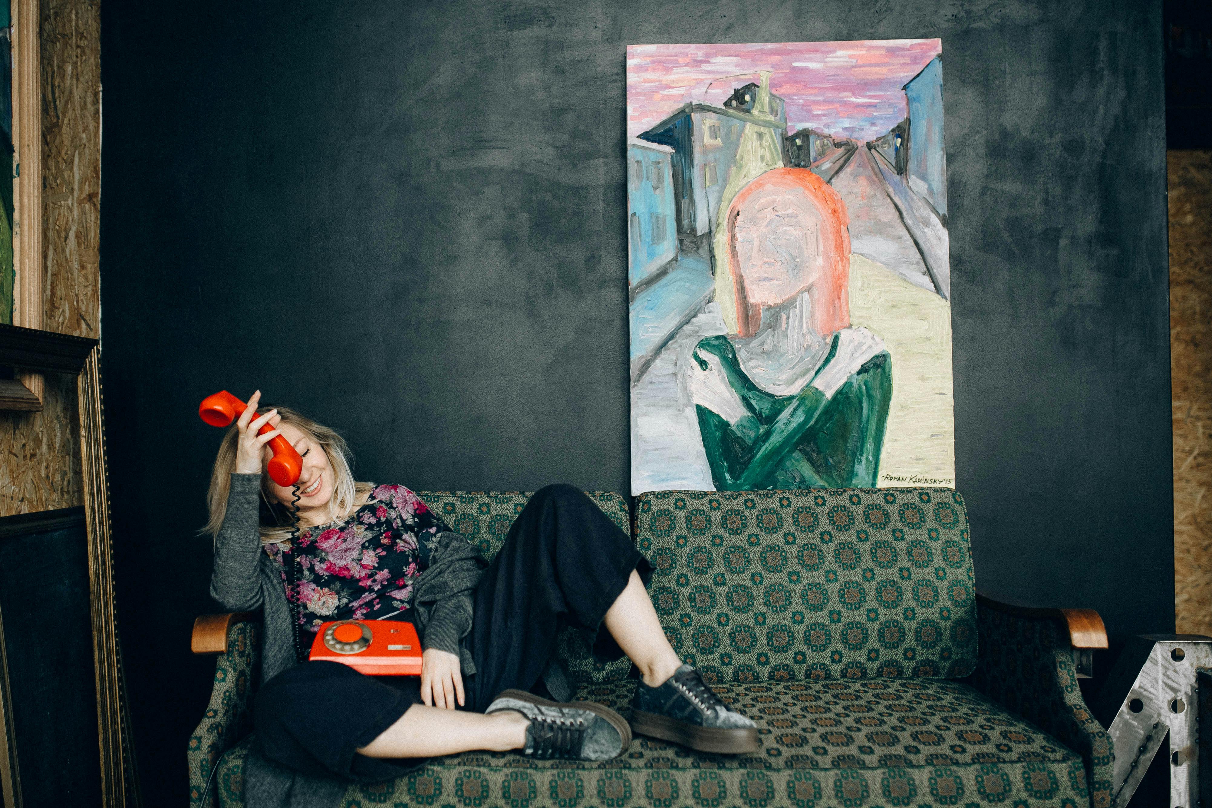 一位妇女懒洋洋地坐在一张老式沙发上，手里拿着一个经典红色电话，背景是反对艺术