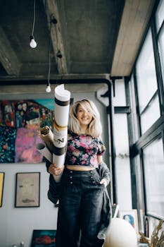Smiling artist in a contemporary studio holding rolled canvases, showcasing creativity.