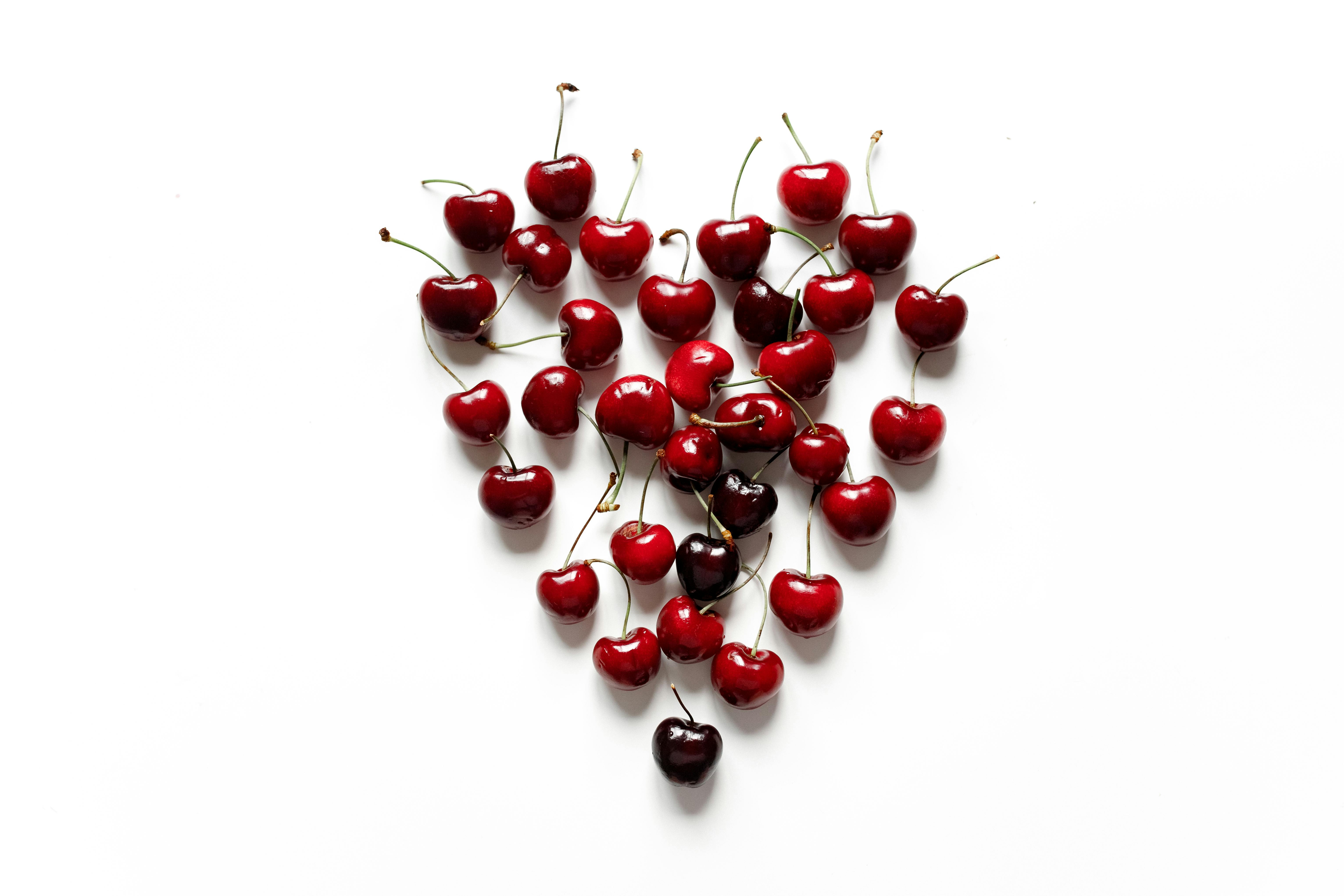 Juicy red cherries arranged in a heart shape on a clean white background, perfect for healthy food concepts.