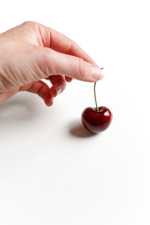 Free Close-up of a hand holding a ripe cherry on a white surface, emphasizing freshness. Stock Photo