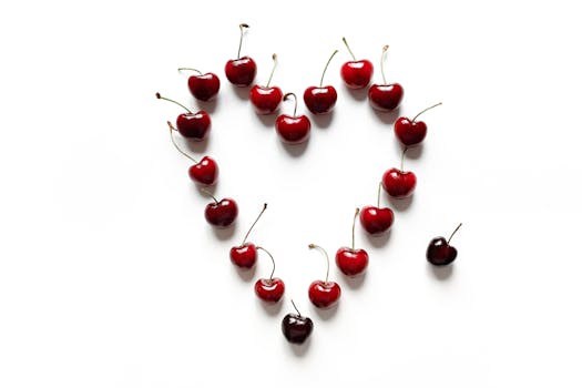 Vibrant red cherries arranged in a heart shape on a clean white background, symbolizing freshness and love.