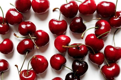 Free Close-up of juicy red cherries scattered on a white surface, ideal for food concepts. Stock Photo