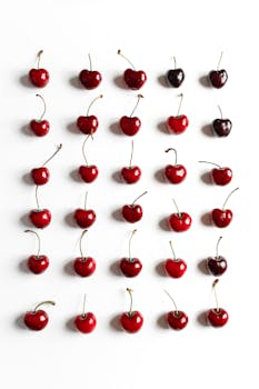 A vibrant display of fresh cherries arranged in a grid on a white surface, highlighting natural beauty.