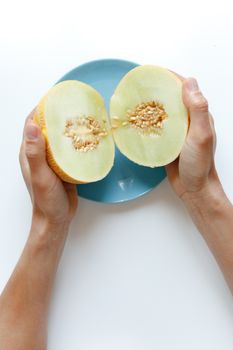 Hands holding fresh honeydew melon halves over a blue plate. Perfect for healthy eating themes.