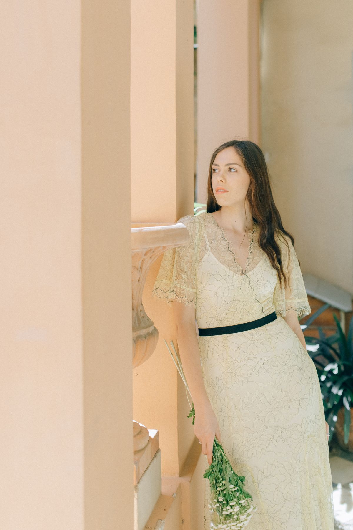 Mulher em vestido vintage de renda em corredor iluminado, segurando buquê de flores brancas