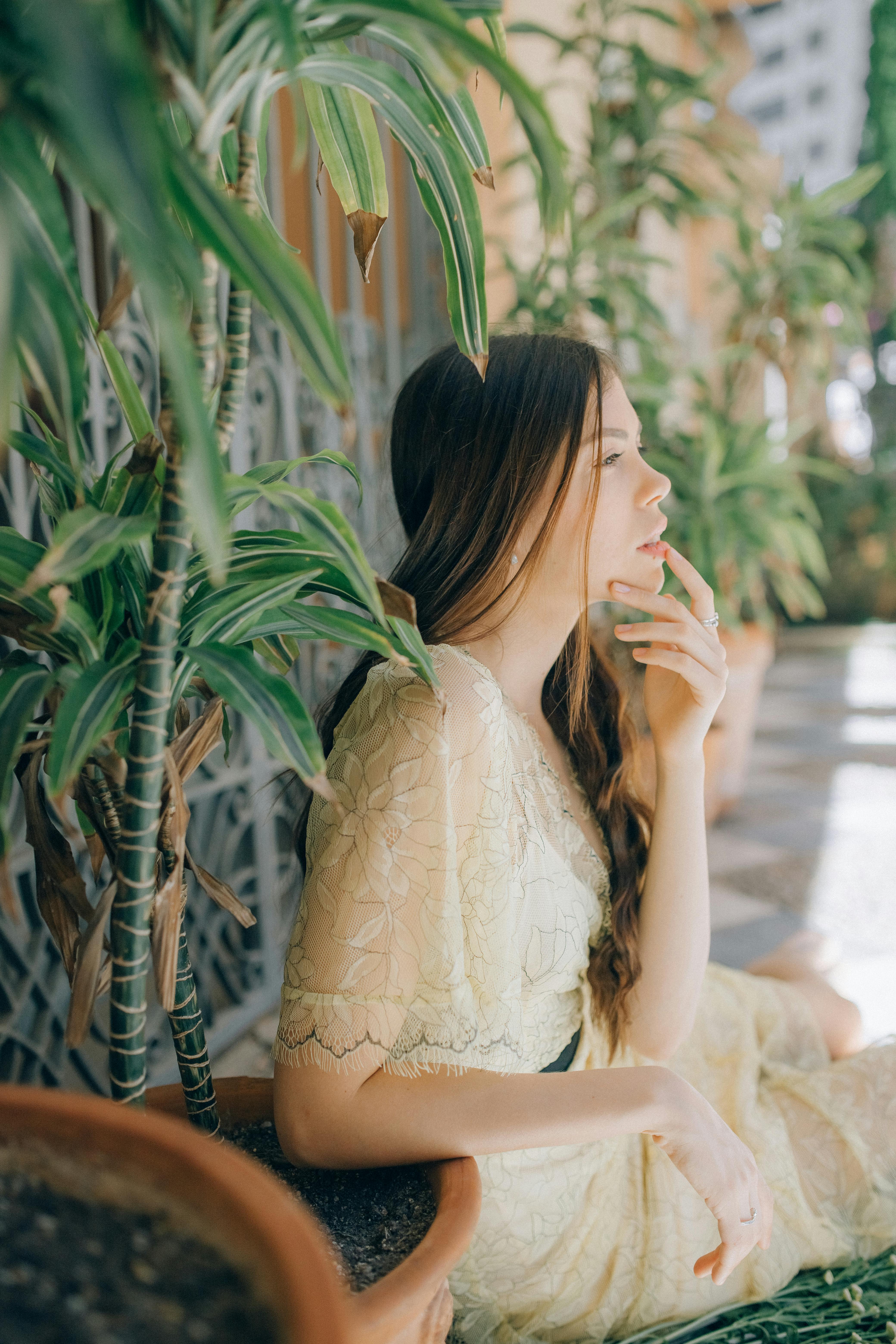A serene side view of a woman in a delicate lace dress, surrounded by potted plants.