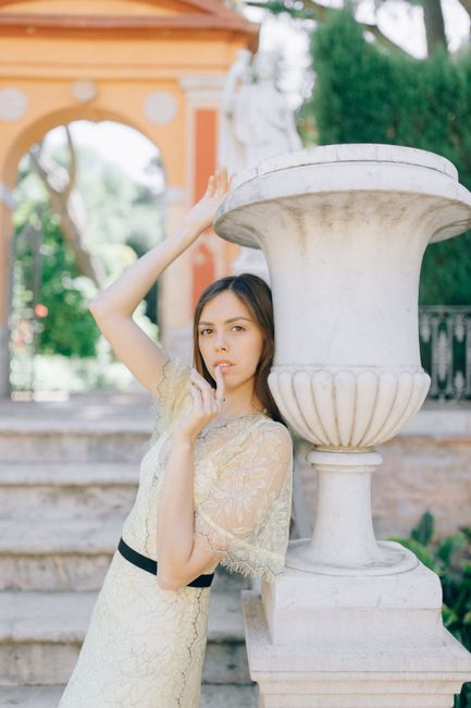 A young woman poses elegantly in a stylish dress in an outdoor setting with classic architecture.