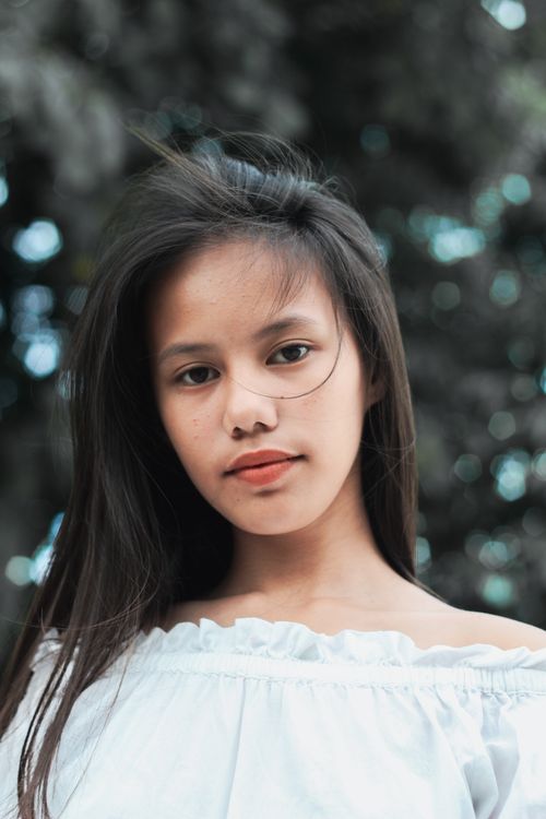 Free Close-up portrait of a young woman with long hair and soft expression against a natural outdoor backdrop. Stock Photo