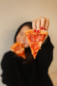 A woman with red nails holding a pepperoni pizza slice, focusing on food.