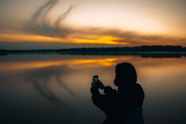 Silhouette Of Person Standing Near A Lake