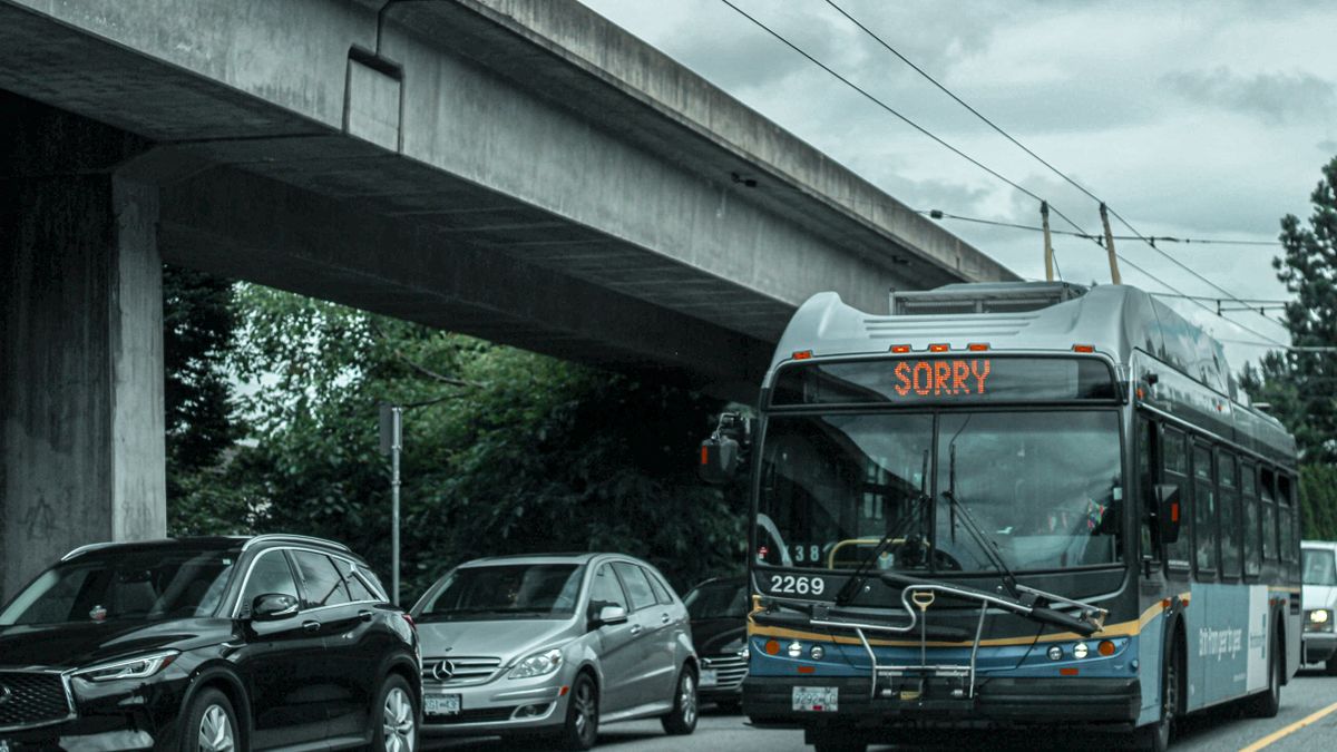 A busy city street with traffic and a bus showing 'SORRY' on its display under an overpass.