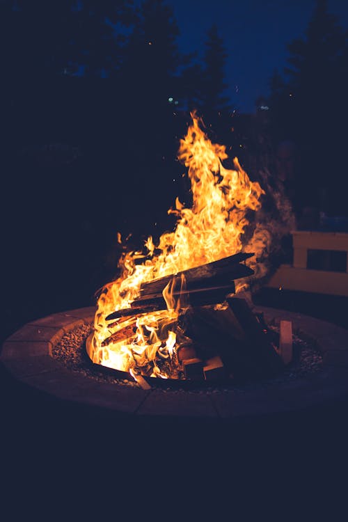 From above of firewood burning in glowing flame in stone fire pit in darkness