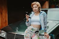 一位穿着复古服装的女性微笑着靠在镀铬汽车上，手持无线手机看向相机