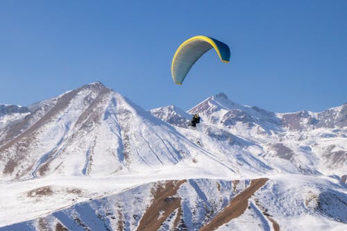 Person in Yellow Parachute over Snow Covered Mountain