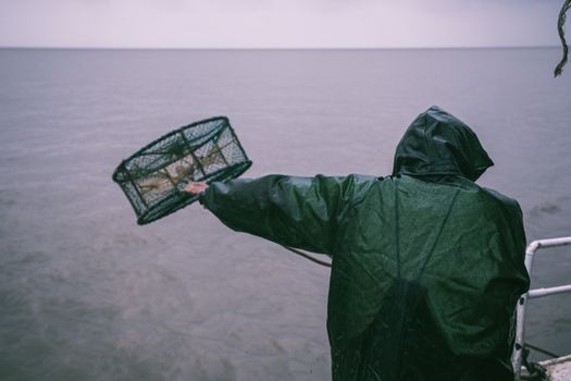 雨天，一名穿着雨衣的渔民将蟹罐扔进海里