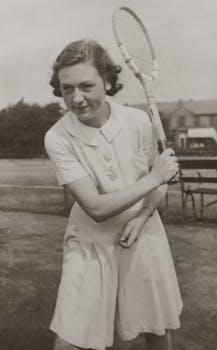 Historic black and white photo of a young woman playing tennis, capturing vintage sports style.