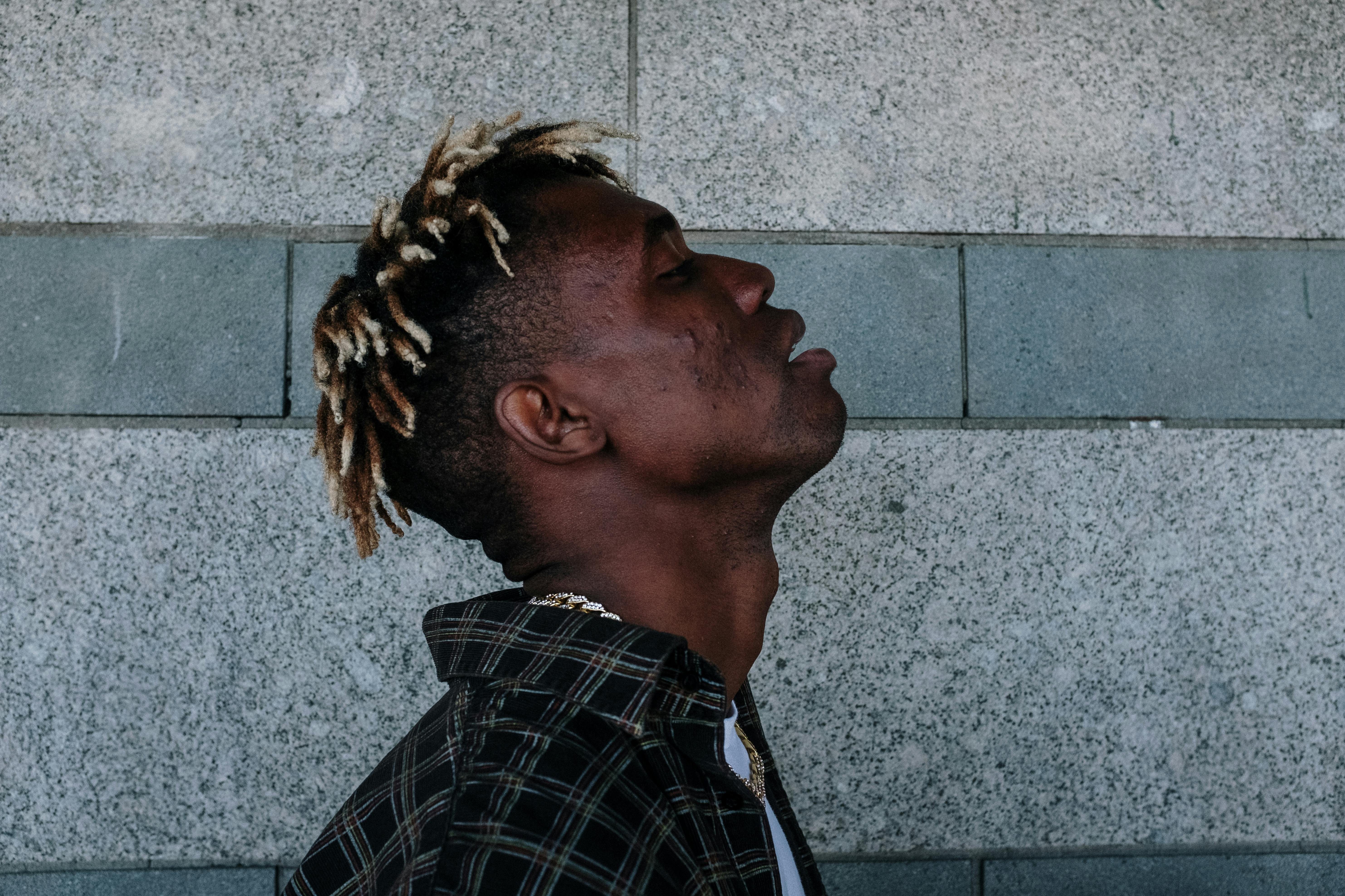 Profile portrait of a stylish man with dreadlocks against a stone wall.