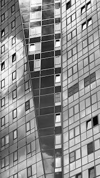Black and white image of a high-rise building with reflective glass windows capturing the sky.