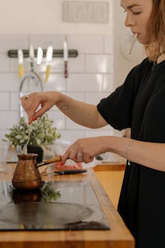 Woman making Turkish coffee on a stovetop in a well-lit kitchen setting.