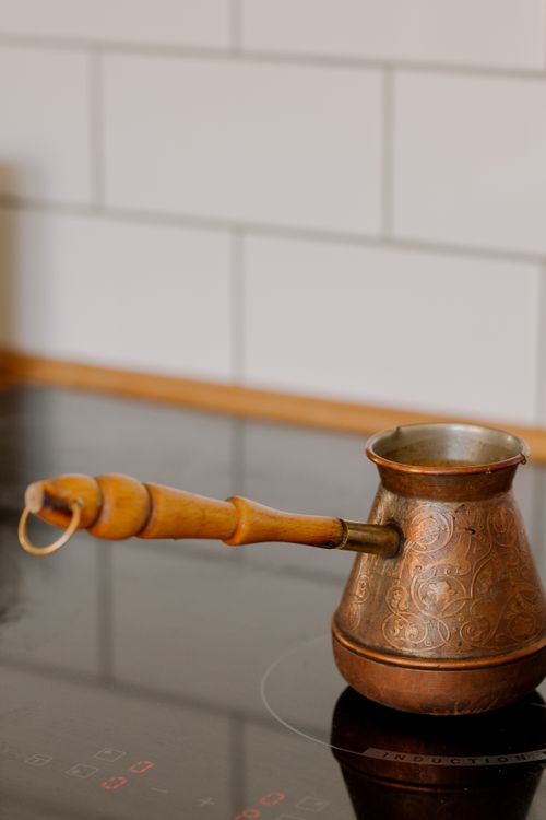 Free Close-up of a copper cezve with intricate designs on a modern kitchen stovetop. Stock Photo