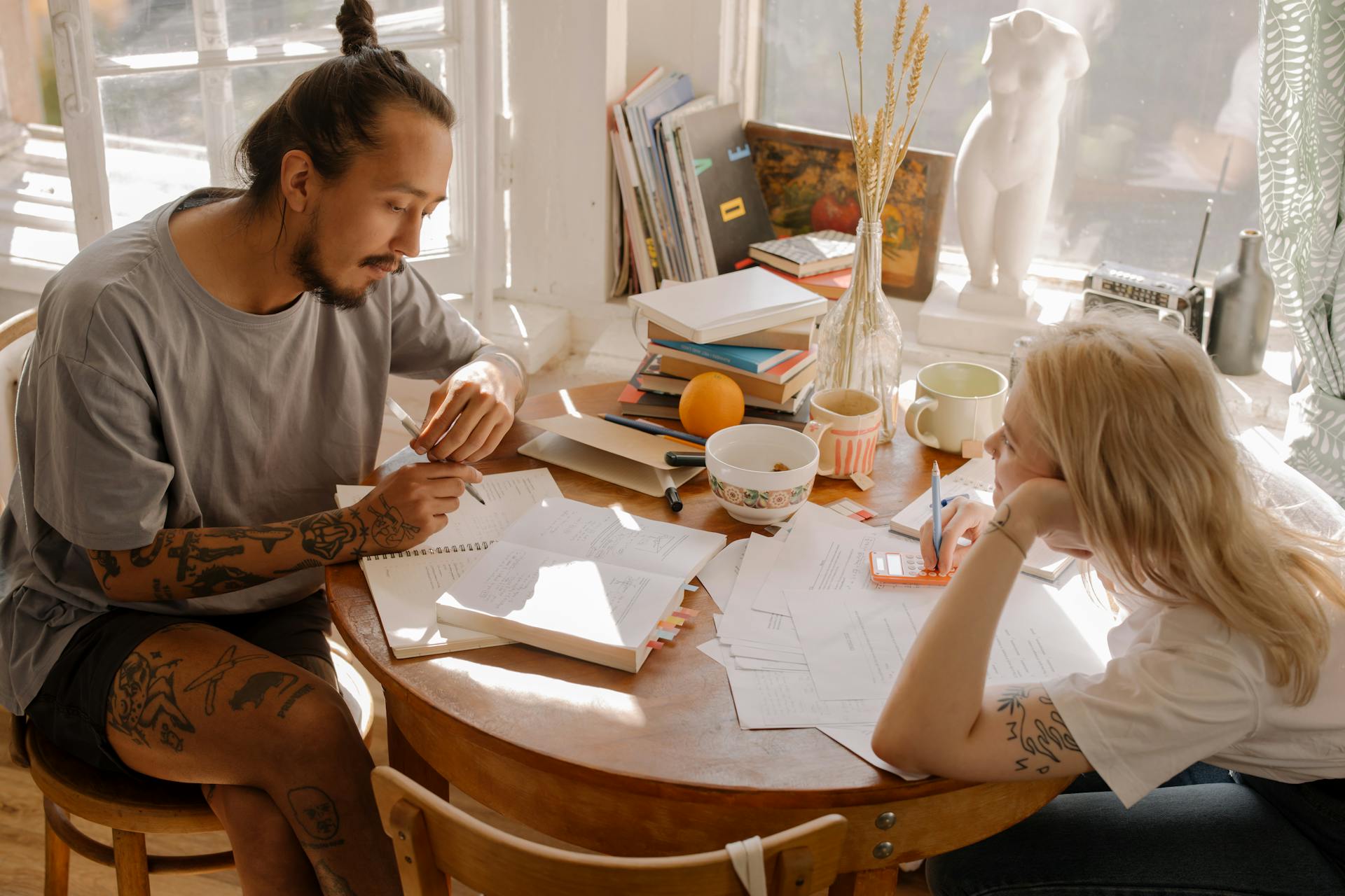 Two students studying with books and notes, collaborating in a cozy space filled with natural light.