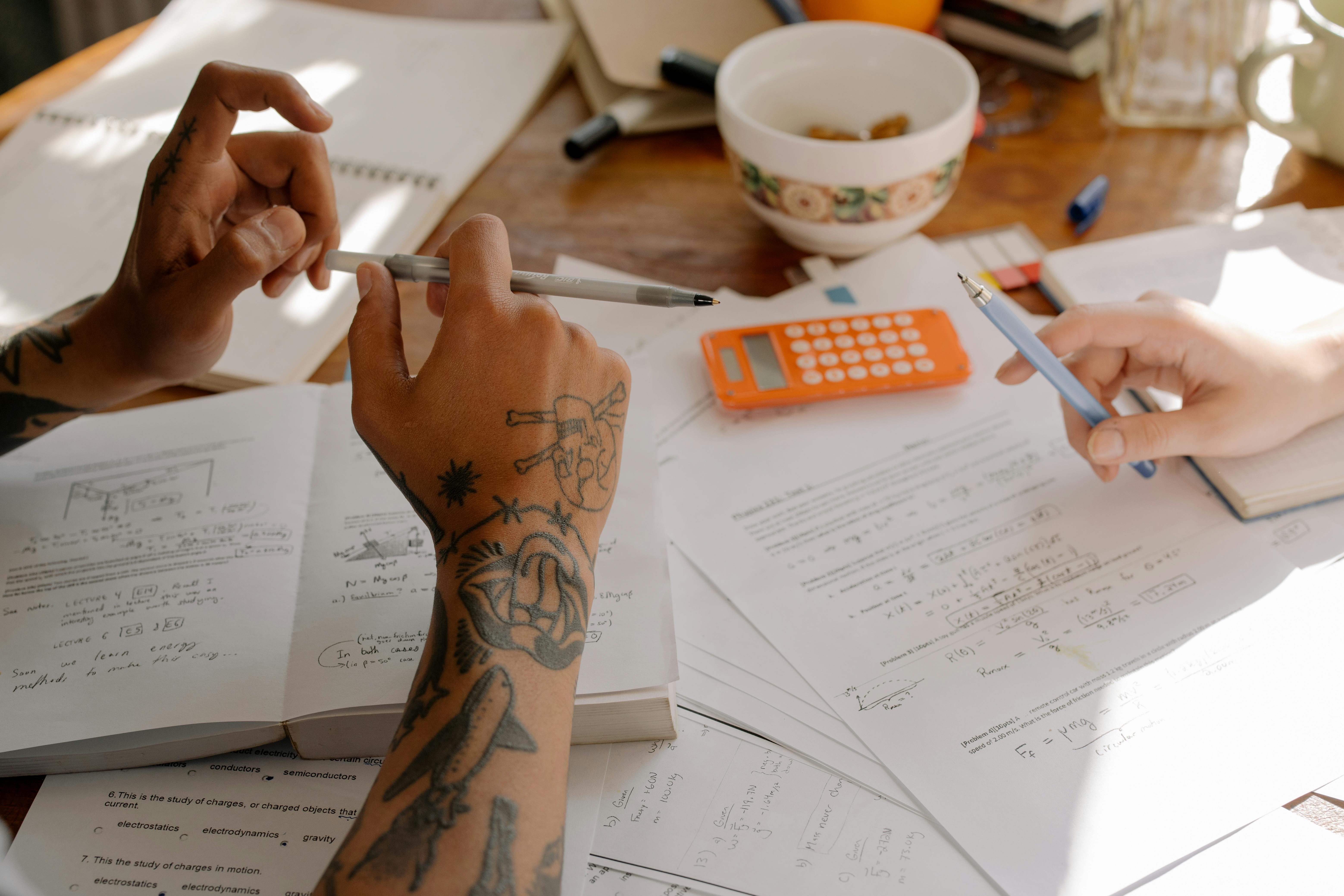 person with tattoo on arm holding pen writing on white paper