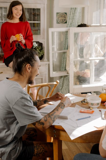 Young tattooed student studying at a sunlit table with friends, engaging in college learning.