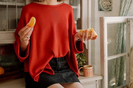 A woman in a red sweater sits in the kitchen, enjoying fresh orange slices.