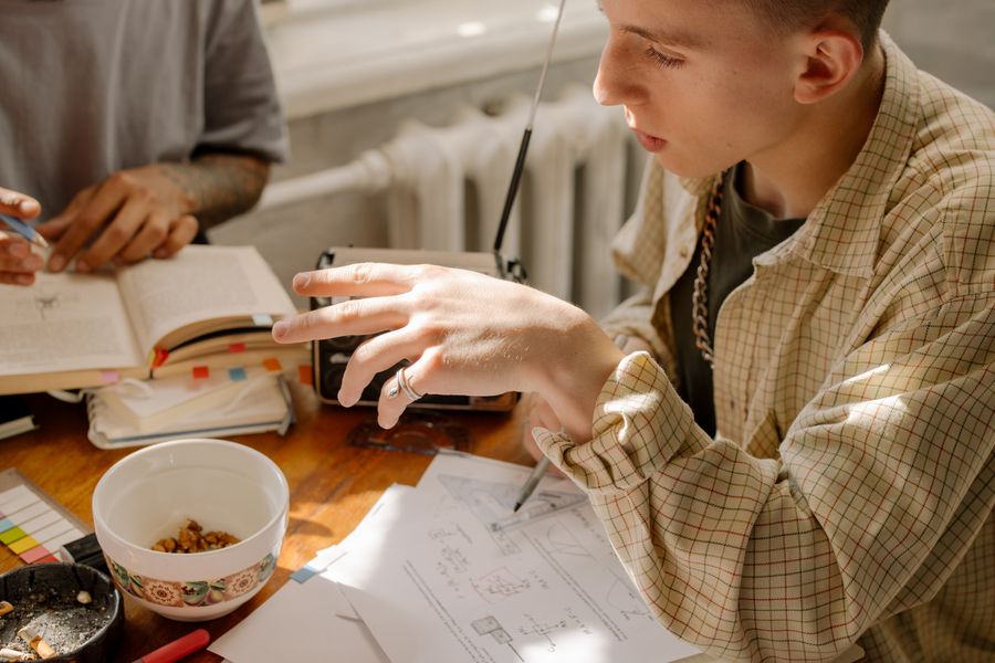 Two young adults studying and working at a sunlit table with books and papers.