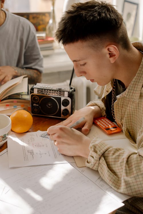 Man in Black and White Plaid Dress Shirt Writing on White Paper