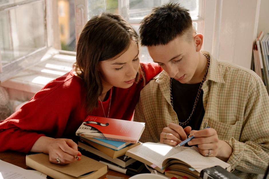 A young couple engaged in studying at a desk with books and notes indoors.