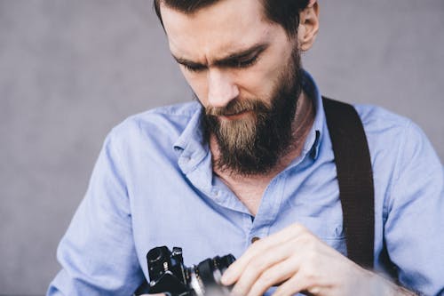 Close-Up Photo of a Man in a Blue Shirt Fixing His Camera