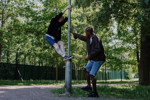 Two friends having fun climbing and playing with a lamppost in a park.