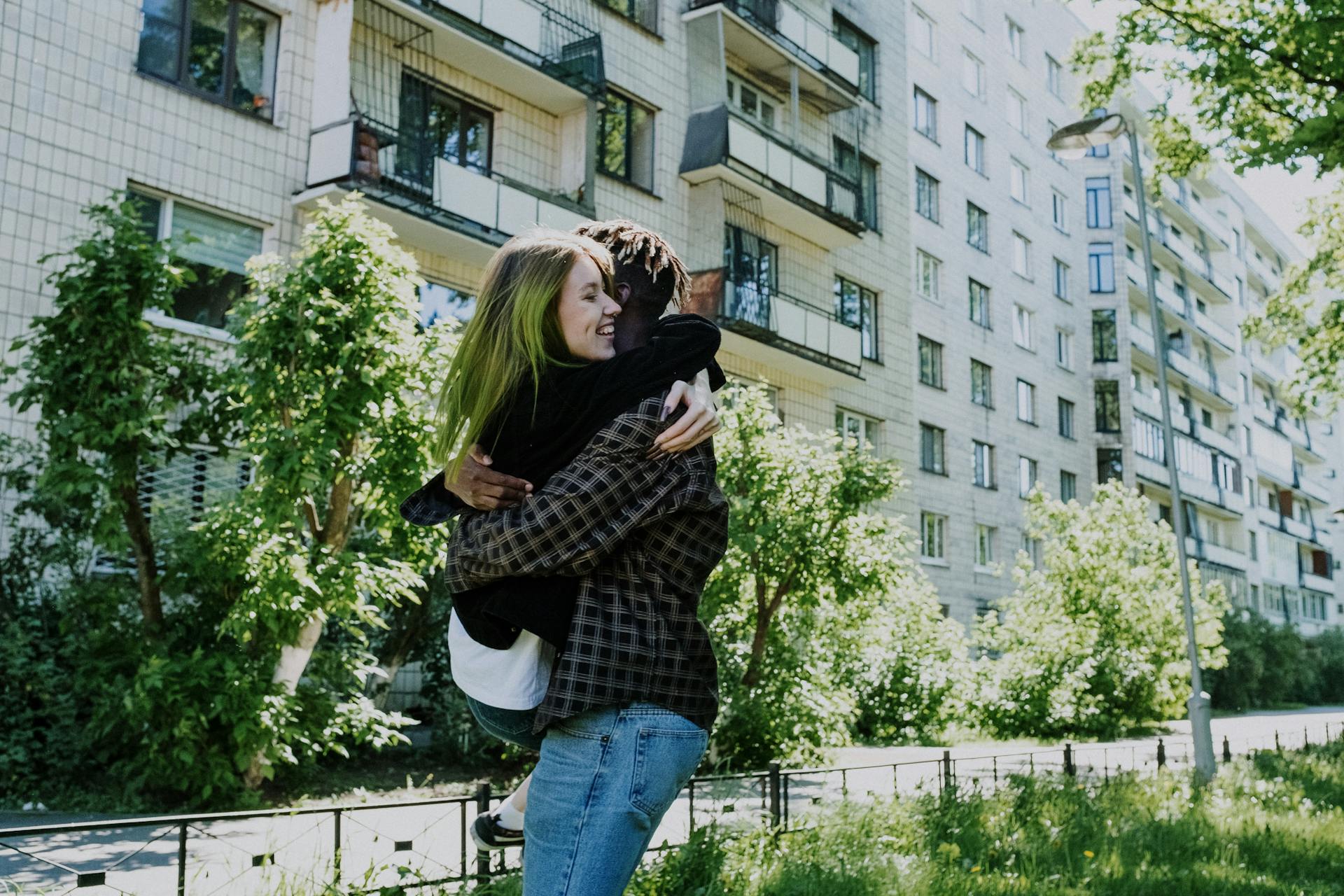 A young couple hugging outside an urban apartment building on a sunny day.