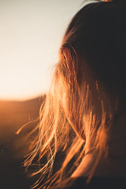 Close-up view of a woman's hair glowing in the golden sunlight, creating a serene and warm atmosphere.