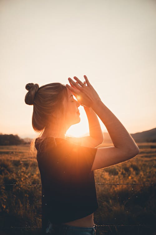 Woman in Black Shirt Standing on Grass Field During Sunset