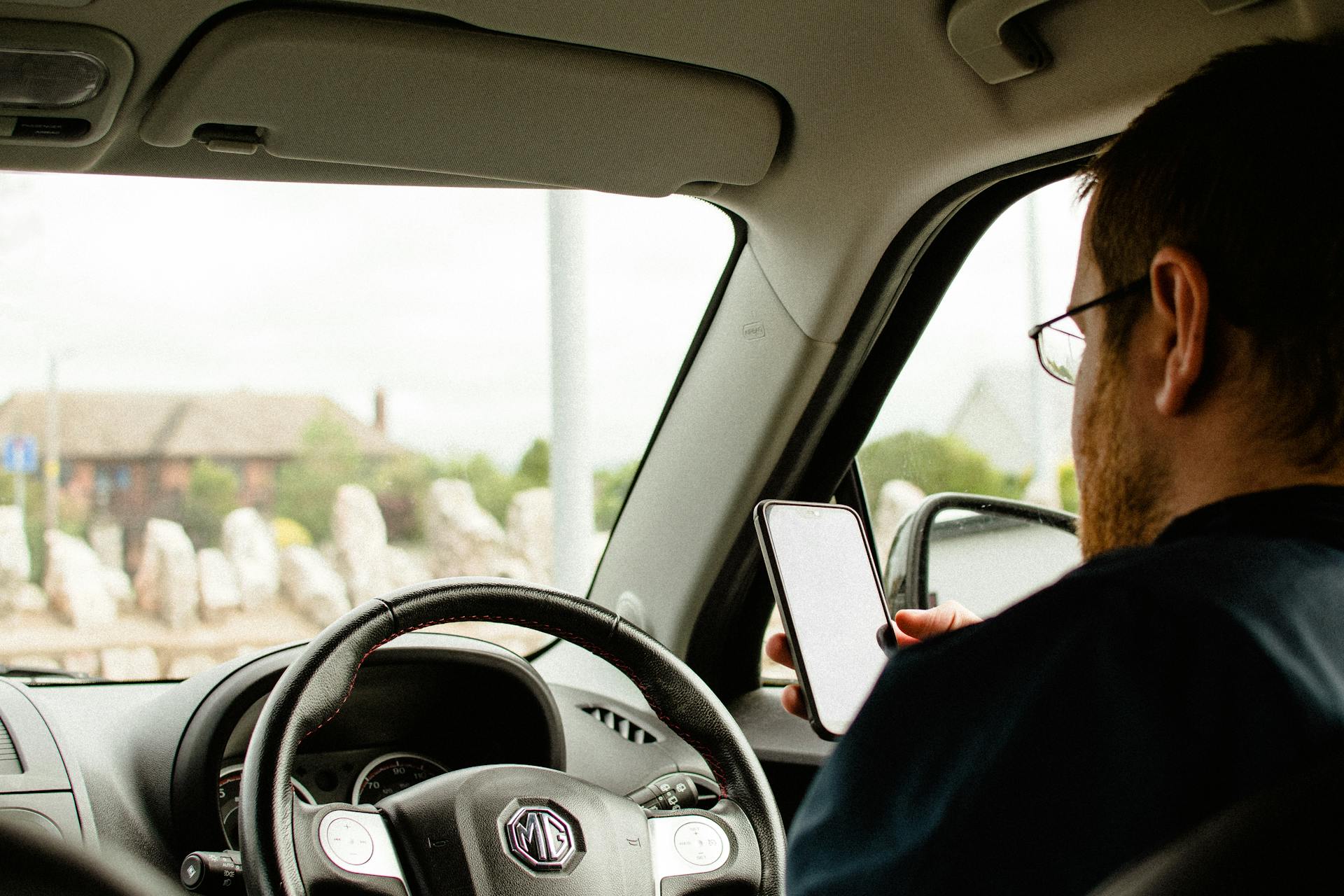 Person in a car using a smartphone with a focus on dashboard and steering wheel.