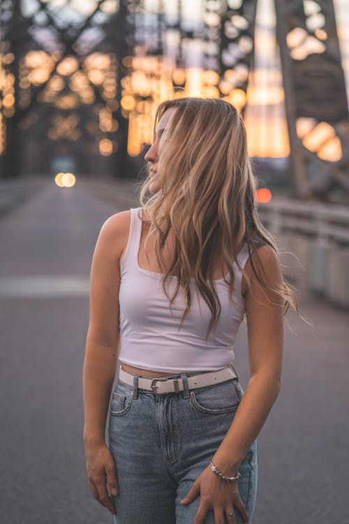 Woman in White Tank Top and Denim Jeans Standing on the Bridge