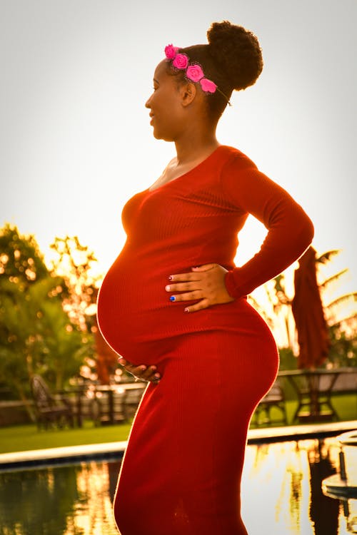 Free Pregnant Woman Wearing Red Dress Standing Near a Pool Stock Photo