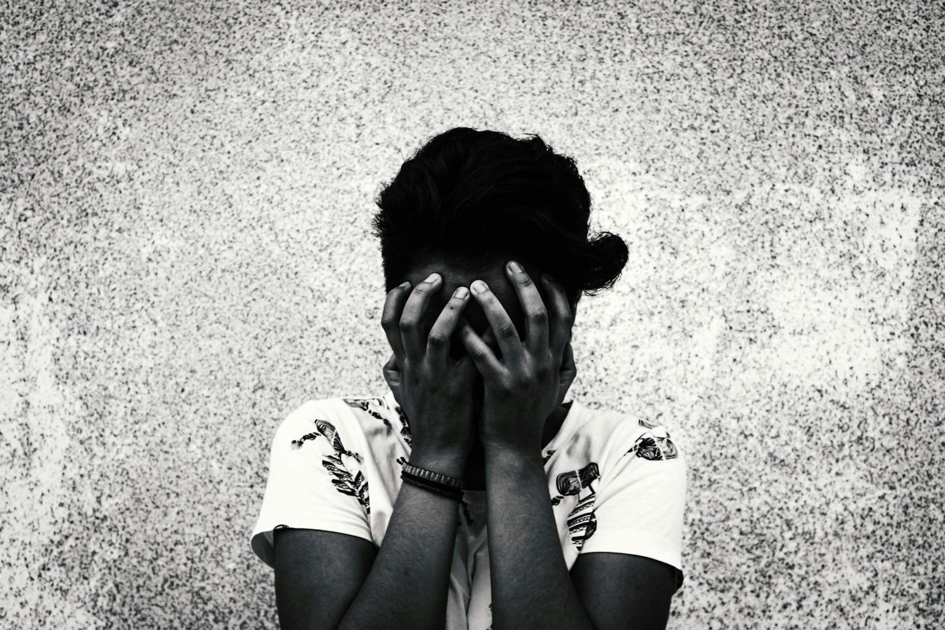 Artistic black and white portrait of a woman covering her face, evoking emotions of sadness or contemplation.