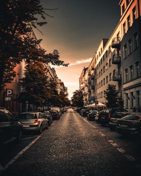 A picturesque urban street lined with parked cars and classic buildings at dusk. Tranquil and charming.
