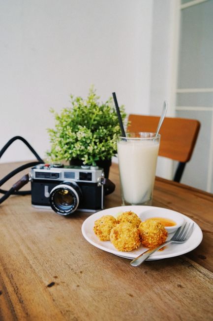 Vintage camera on a wooden table with a plate of snacks and a glass of milk, creating a cozy cafe ambiance.