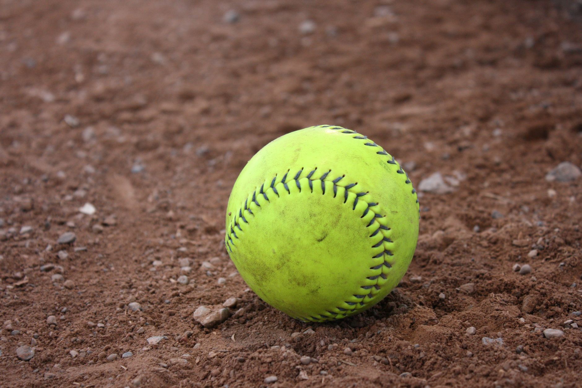 Bright yellow softball resting on a textured dirt field, perfect for sports themes.
