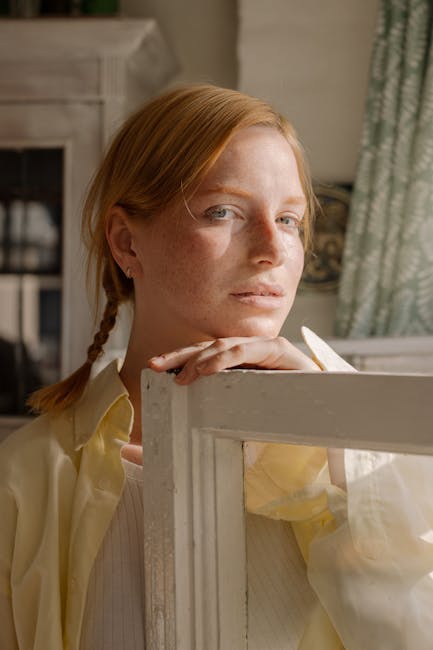 A serene indoor portrait of a redheaded woman with freckles resting on a door frame.