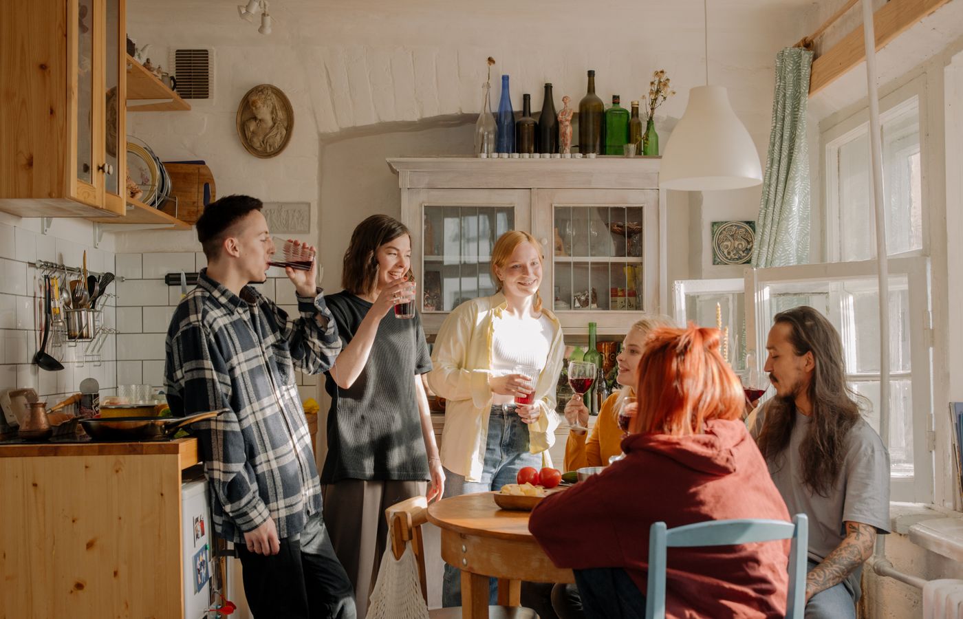 A group of friends laughing and enjoying drinks in a cozy kitchen setting.