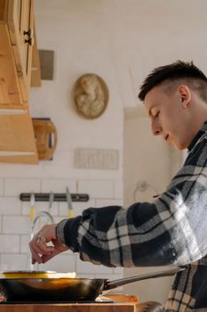 Profile of a young man cooking in a sunlit kitchen with a modern aesthetic.